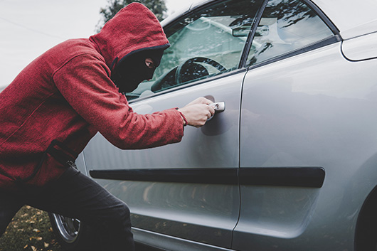 Image of a car thief attempting to break into a vehicle.